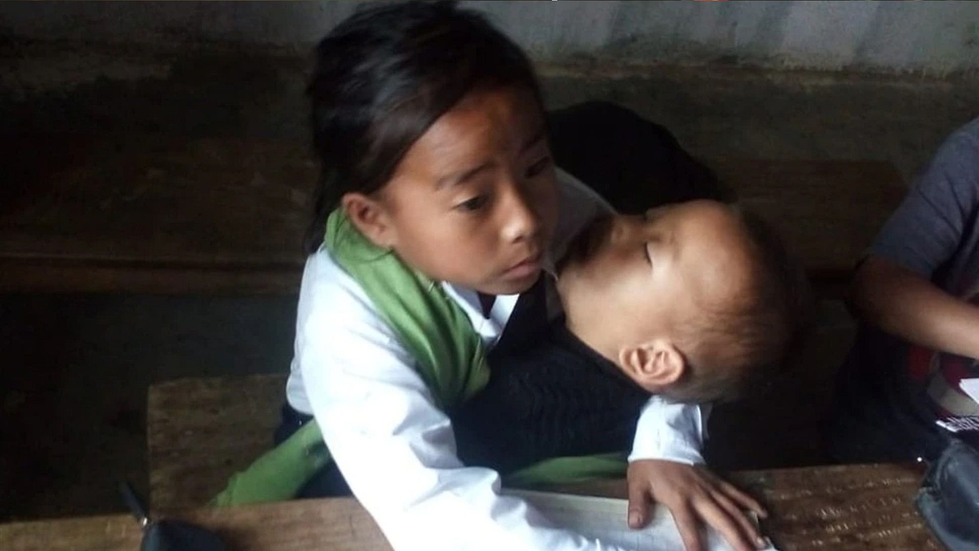Girl reached the school to study with two year old younger sister in her lap