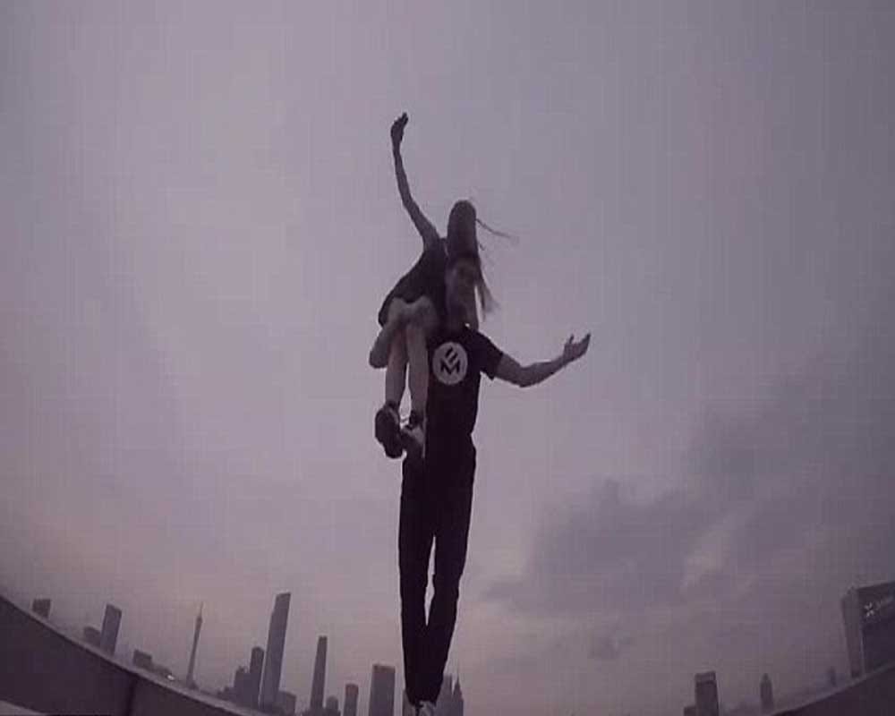 woman dangles from the edge of a skycraper as her boyfriend clings onto one arm 