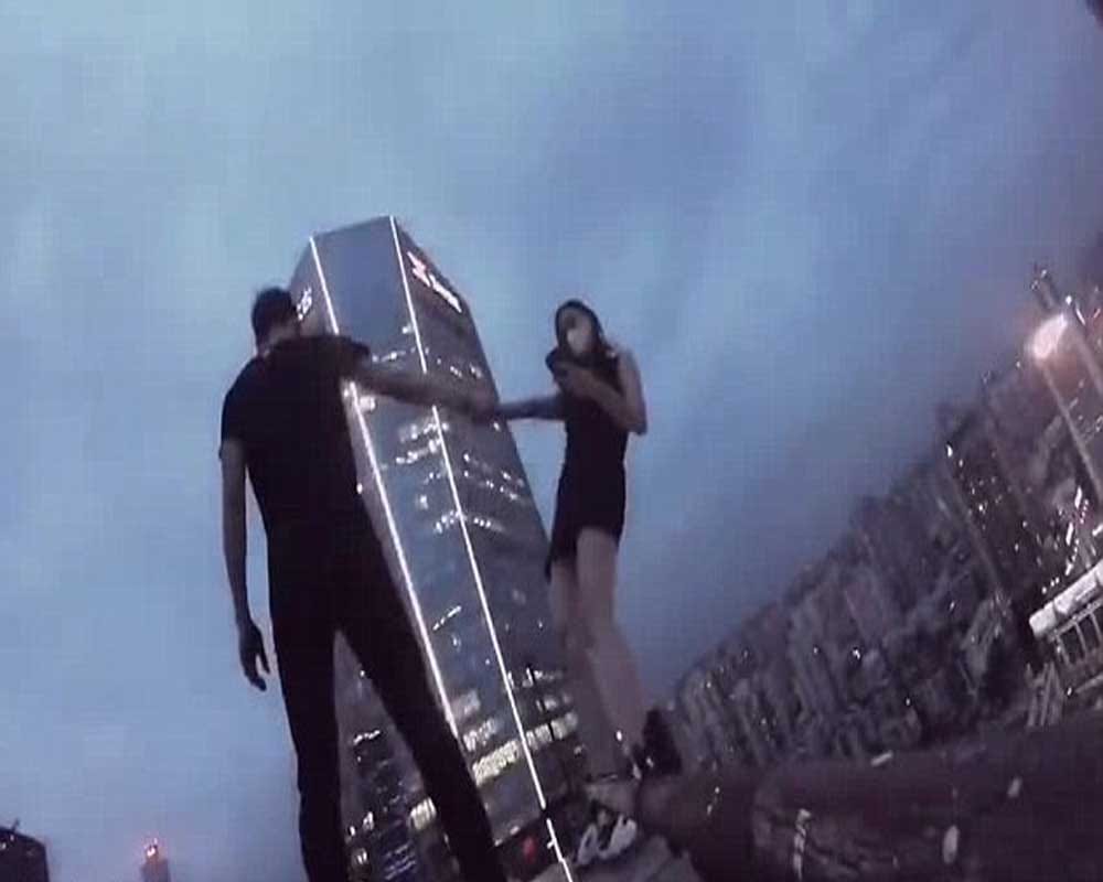 woman dangles from the edge of a skycraper as her boyfriend clings onto one arm 