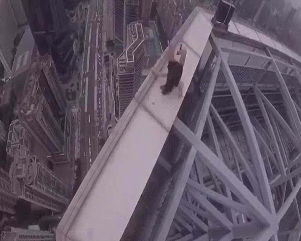 woman dangles from the edge of a skycraper as her boyfriend clings onto one arm 