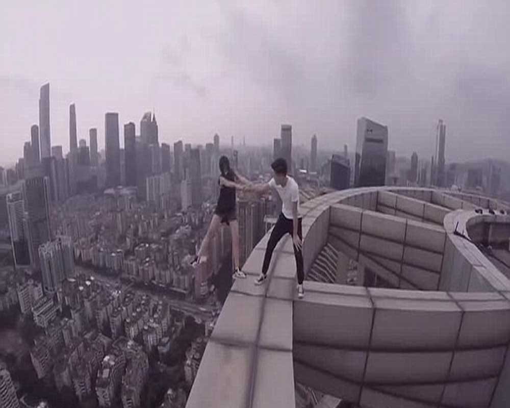 woman dangles from the edge of a skycraper as her boyfriend clings onto one arm 