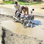 मुहाना में बस स्टैंड पर गड्ढे में गिरी बाइक संभालते लोग।