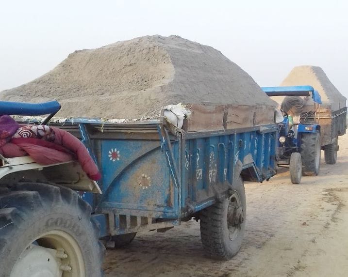 Two tractor-trolley loaded with sand by villagers holding