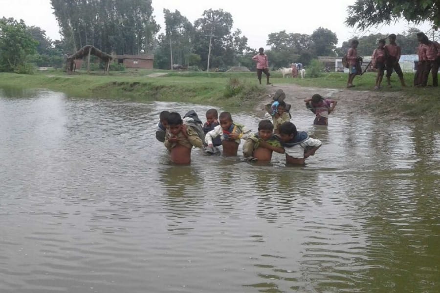 children cross flood water to reach school.