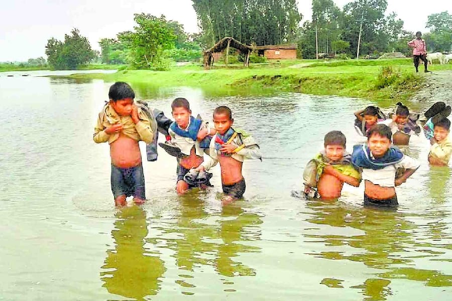 children cross flood water to reach school.