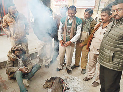 तहसील परिसर में जल रहे अलाव में आग तापते लोग।