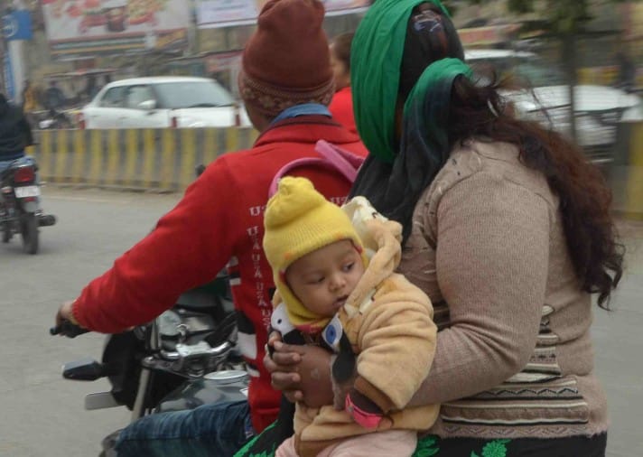 ठंड पडने से बच्चे को गर्म कपडे़ पहनाकर जाती युवती