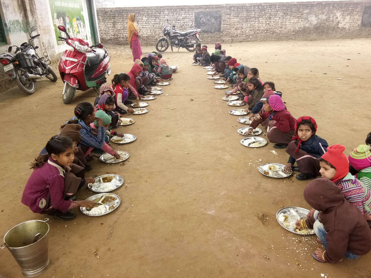 The children sit on the ground and eat food