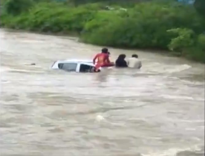 Locals pull a family to rescue using a rope after the family car was submerged in water