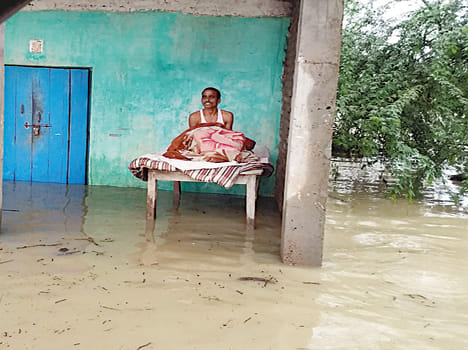  घर के अंदर पानी भरे होने के कारण चारपाई पर बैठा ग्रामीण।