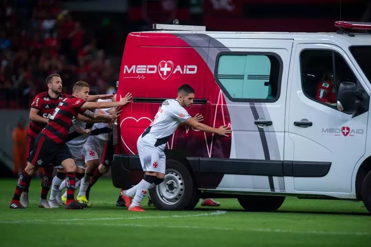 football rival team players get together to push ambulance for injured player