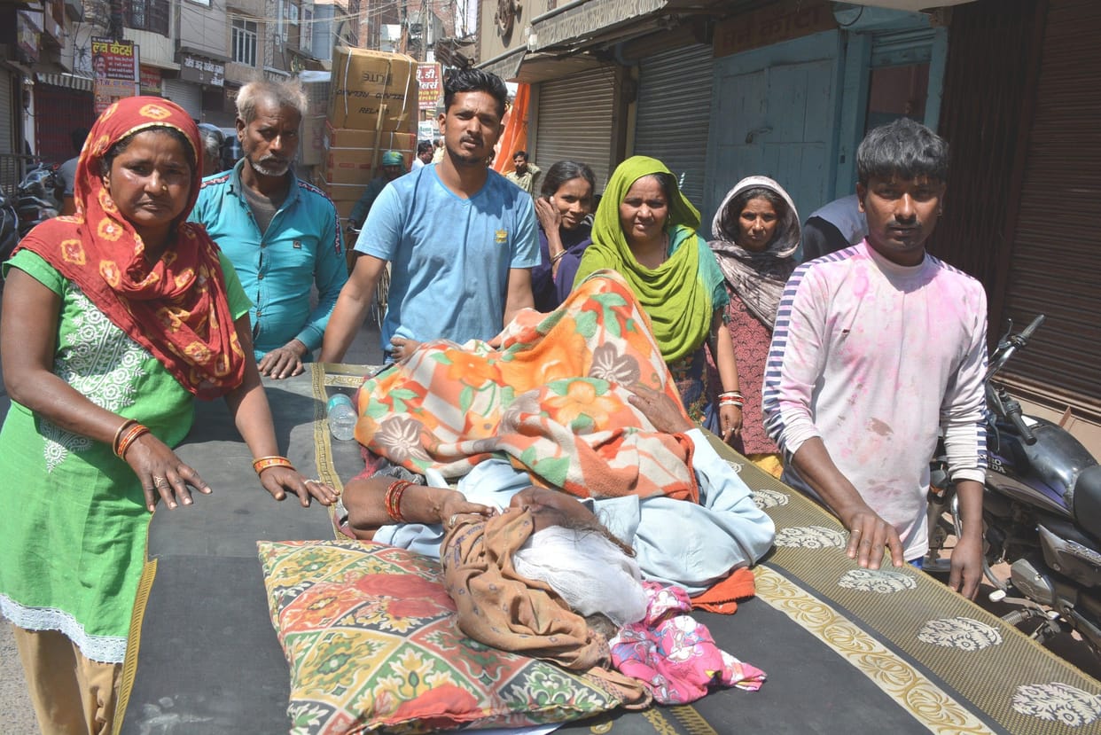 family members walking around pushing an old wounded  woman on trolley.