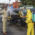 मुंबई बांद्रा रेलवे स्टेशन के पास एक पुलिस कर्मी के शरीर पर दवा का छिड़काव करता सफाई कर्मी।