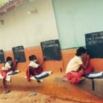 दीवार पर बने ब्लैकबोर्ड से पढ़ाई करते बच्चे