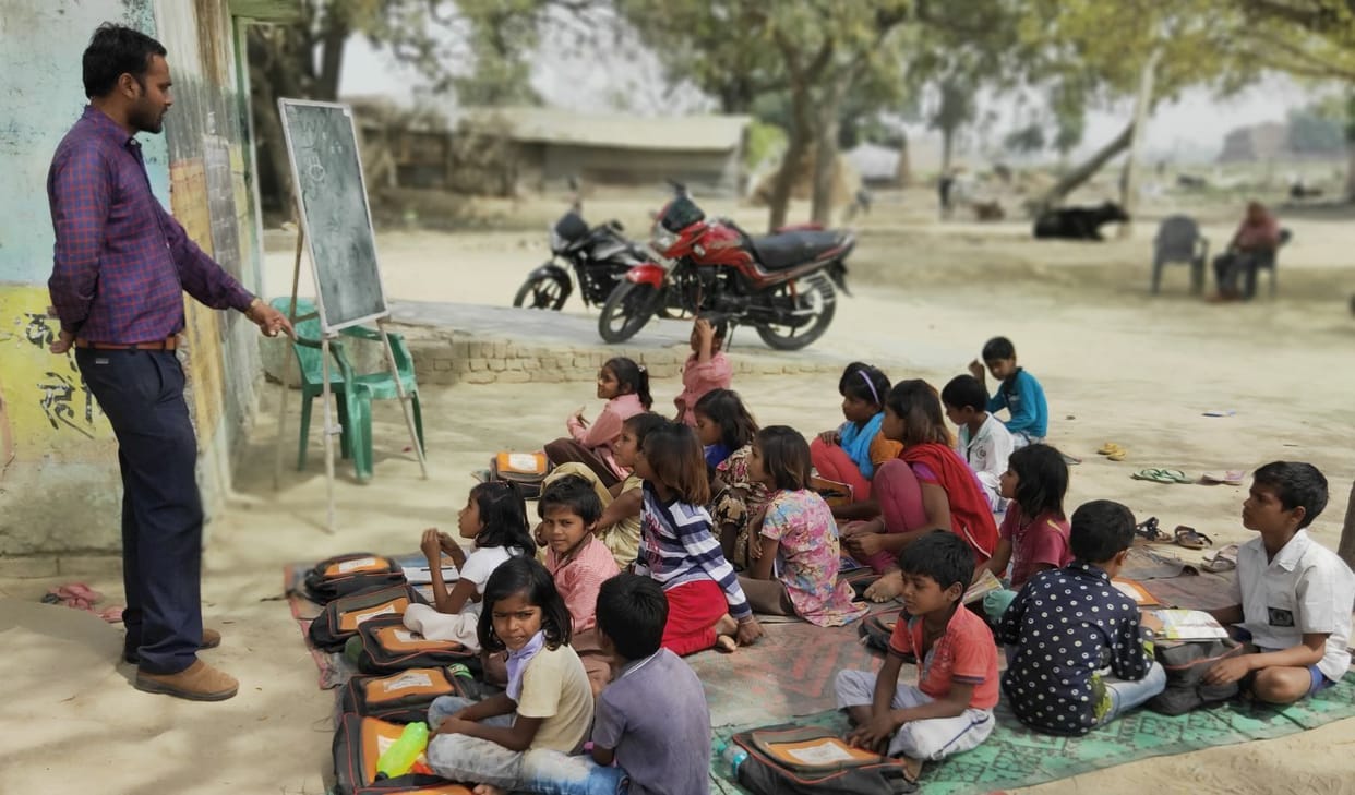 No buildings in school, children sitting in the open