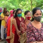 वैक्सीन लगवाने के लिए लाइन में खड़े होकर अपनी बारी आने का इंतजार करतीं महिलाएं।