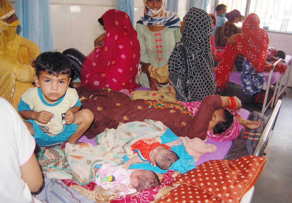 Three patients on one bed, mothers sit on the floor with the baby in their lap