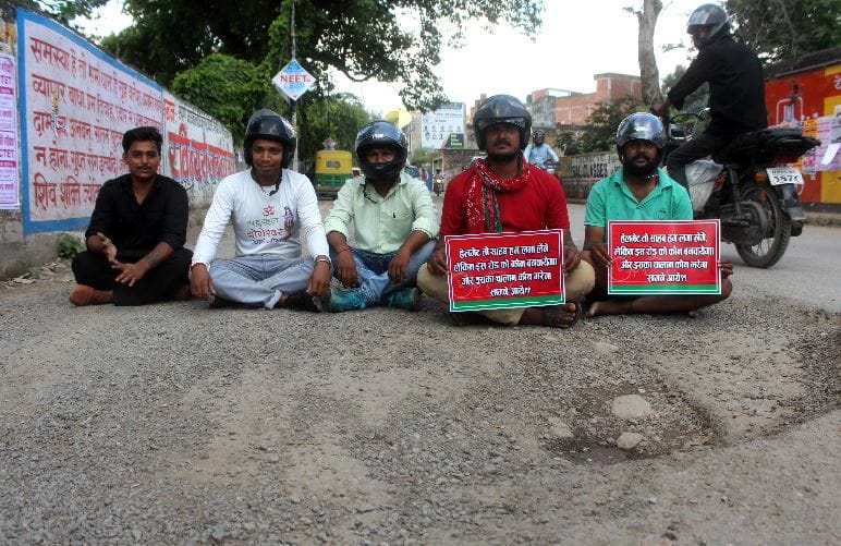 Samajwadi Party workers by sitting in pit of road, protest by wearing helmets
