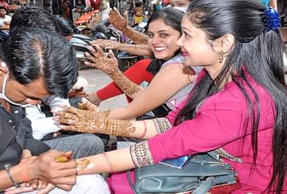 करवा चौथ 2021: हाथों पर मेहंदी रखवाती महिलाएं