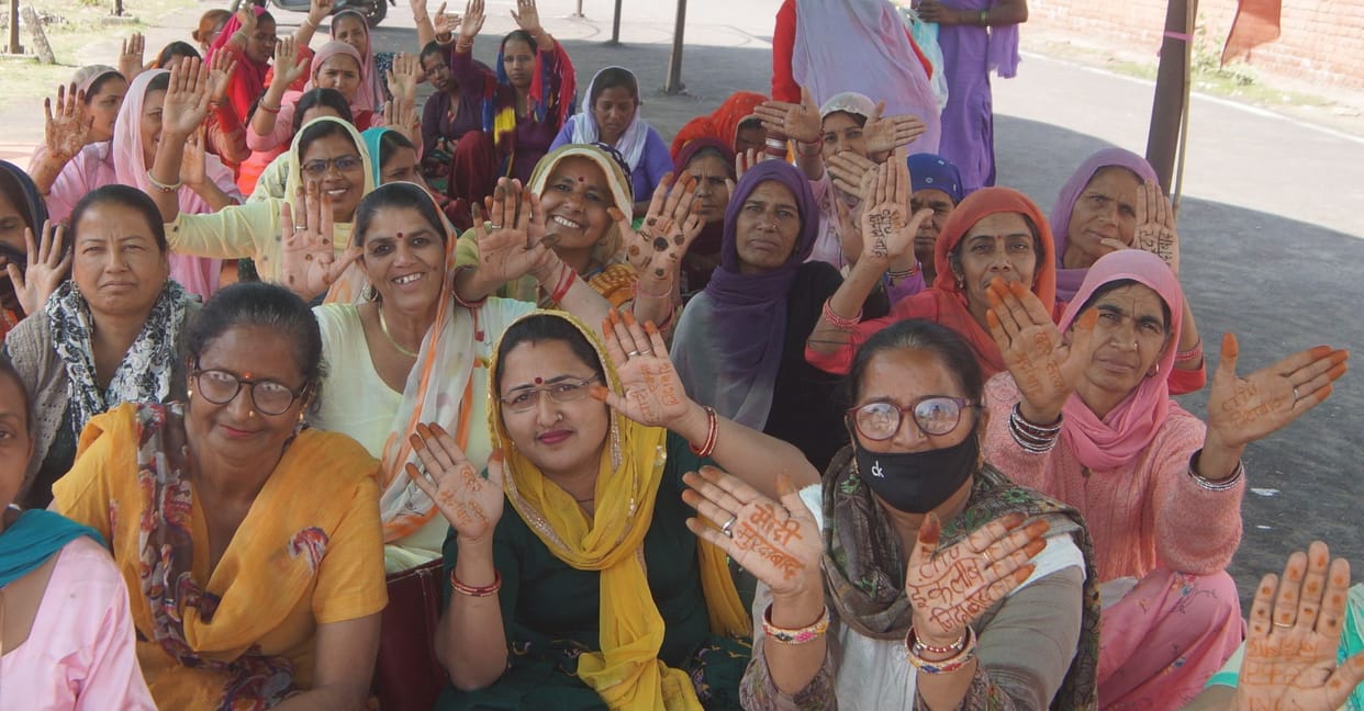 Anganwadi workers and helpers protest by writing slogans with henna on their hands