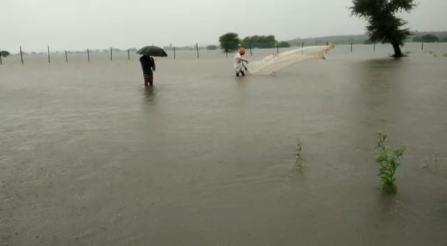 तेज बहाव के बीच मछलियां पकड़ते हुए लोग।