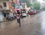 कचहरी रोड पर बूंदाबांदी में छाता लगाकर गुजरता राहगीर ।