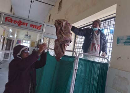 गोंडा में जिला अस्पताल के चिल्ड्रेन वार्ड के सामने खिड़की पर पर्दा लगाता स्वास्थ्यकर्मी। -