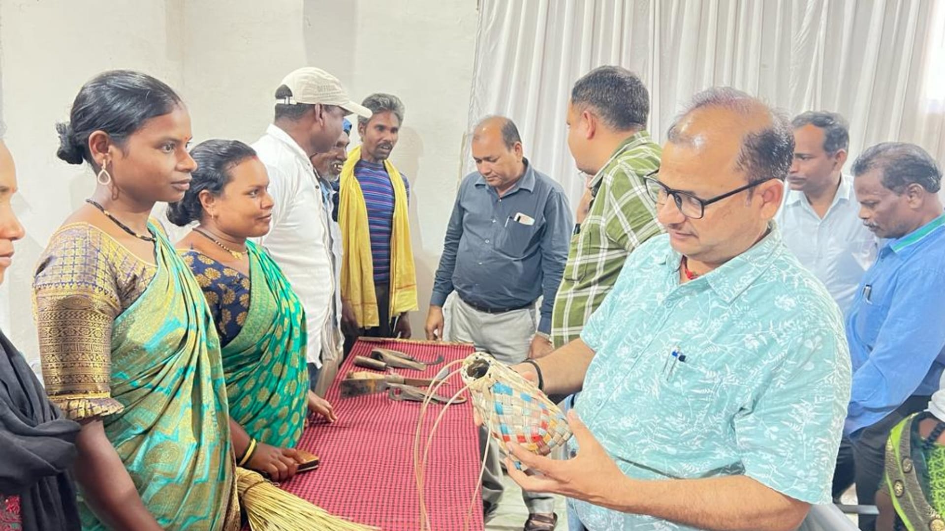 आदिवासी कारीगर मेले में कलात्मक वस्तुएं देखते लोग।