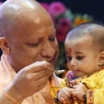 कार्यक्रम में एक बच्चे का अन्न प्राशन करवाते मुख्यमंत्री योगी आदित्यनाथ।