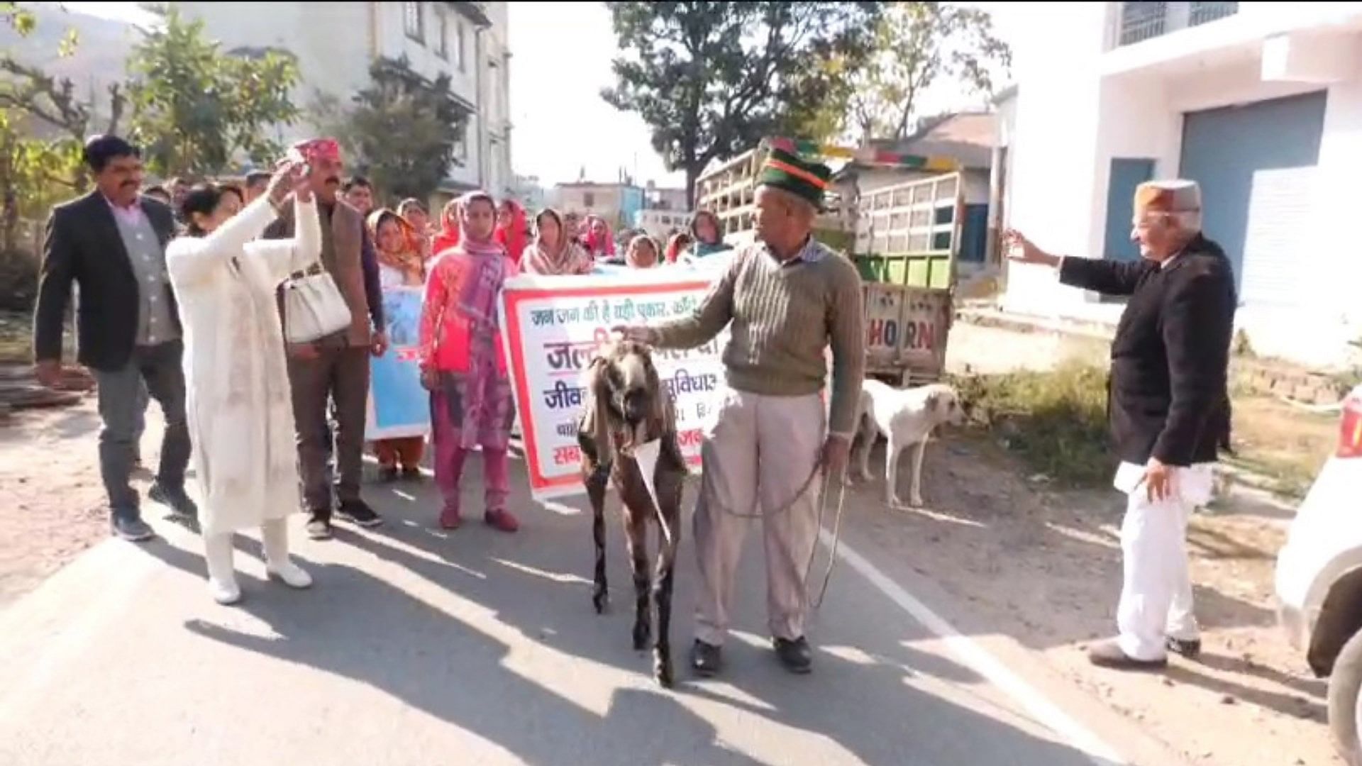 बकरे के गले में पोस्टर बांधकर प्रदर्शन करते लोग।