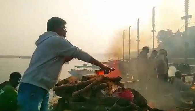 वाराणसी के मणिकर्णिका घाट पर चिता पर लेटे पिता के शव को शराब अर्पित करता पुत्र।