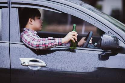 Man holds a beer bottle while is driving a car