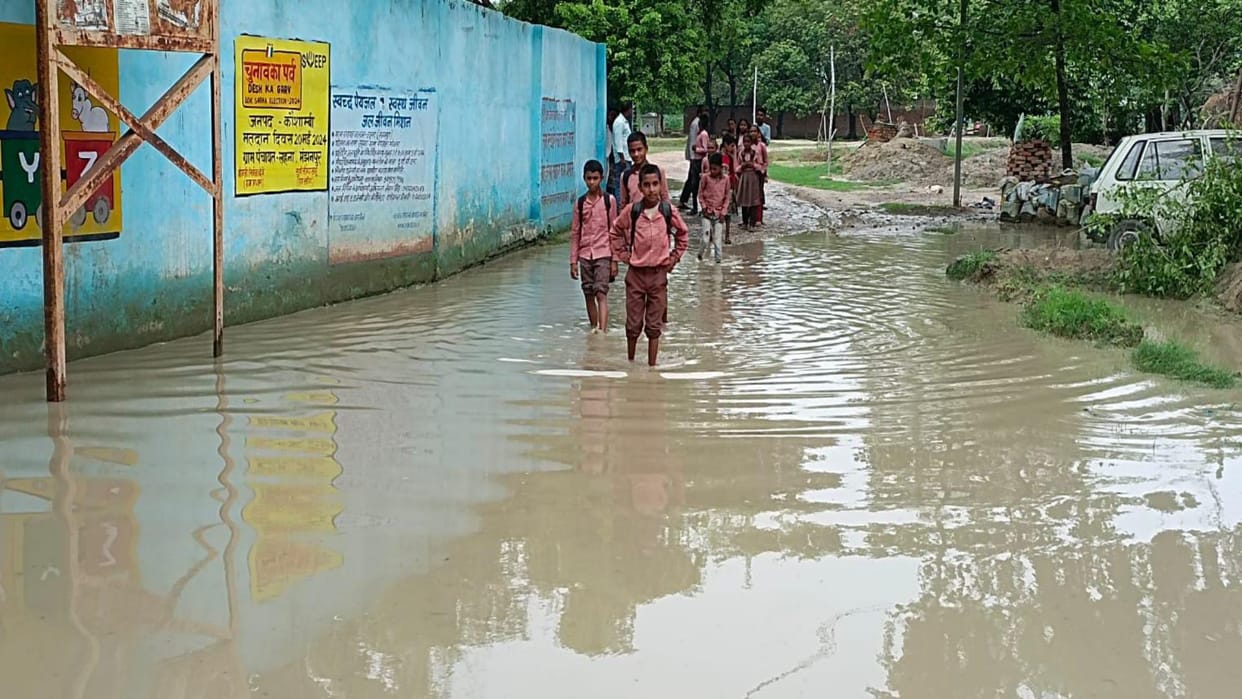 Road to school filled with rain water, school children wade through water to reach school