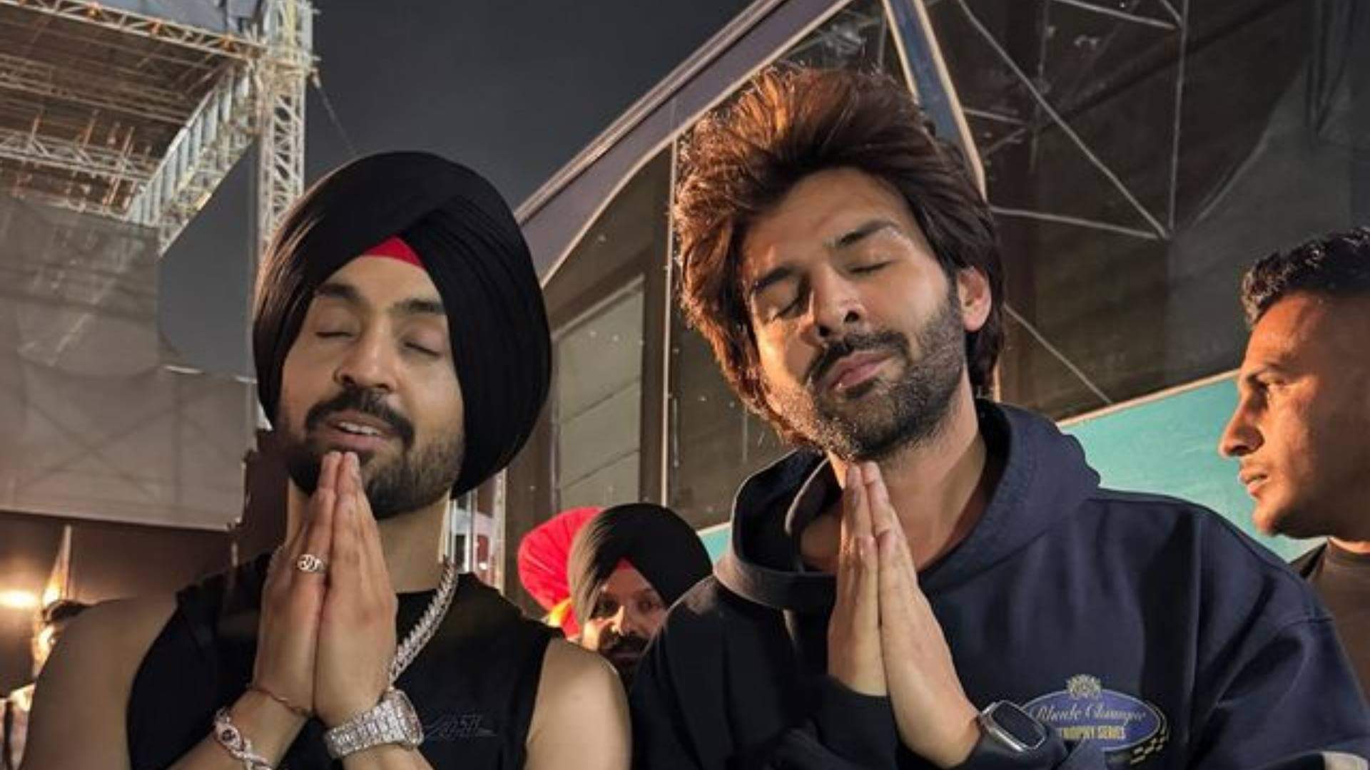Diljit Dosanjh and Kartik Aaryan raising their hands as they twinned in black outfits at Ahmedabad show