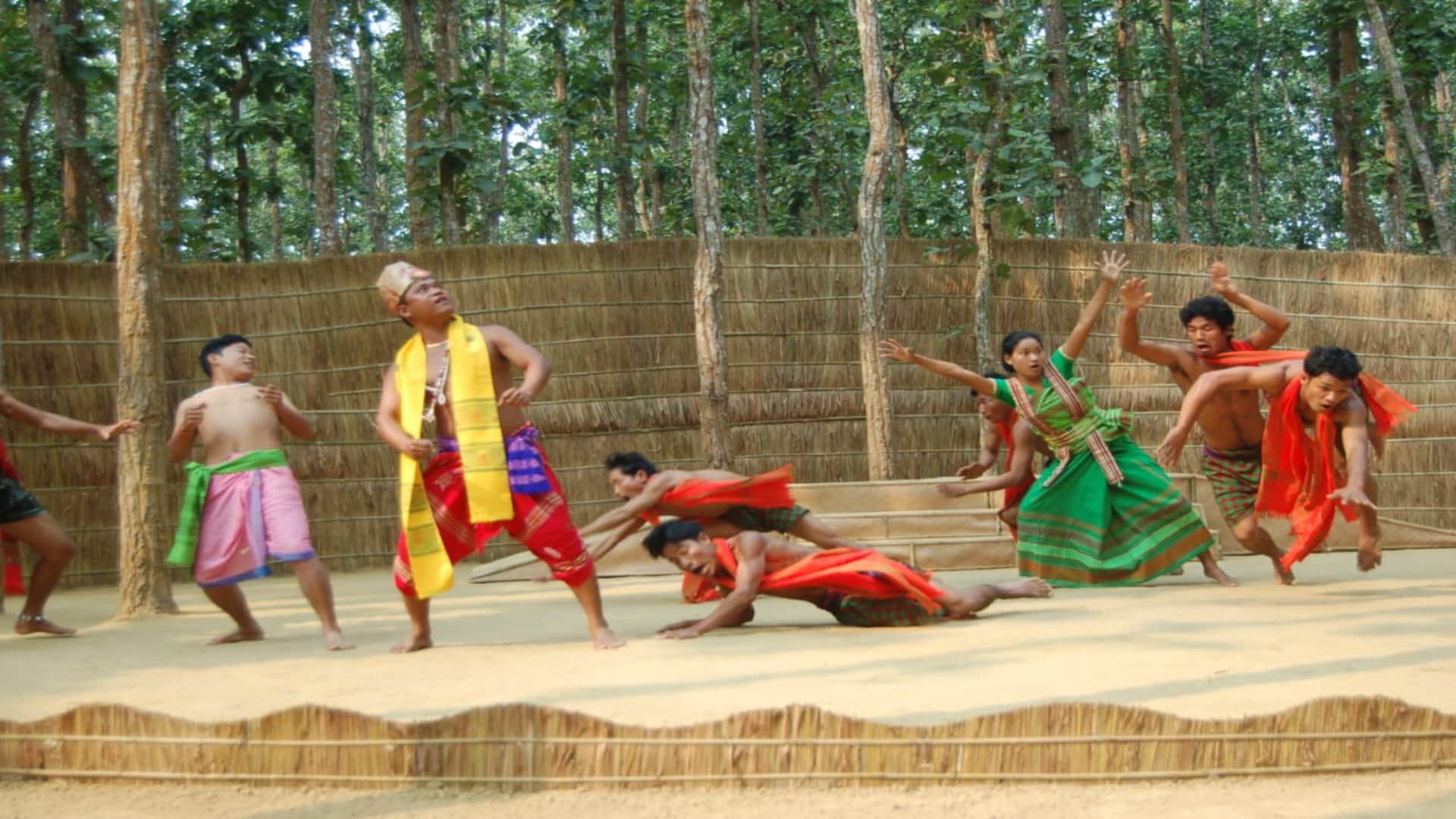 Under the Sal Tree Theatre Festival: Open stage under the trees, audience sits on straw; see picture