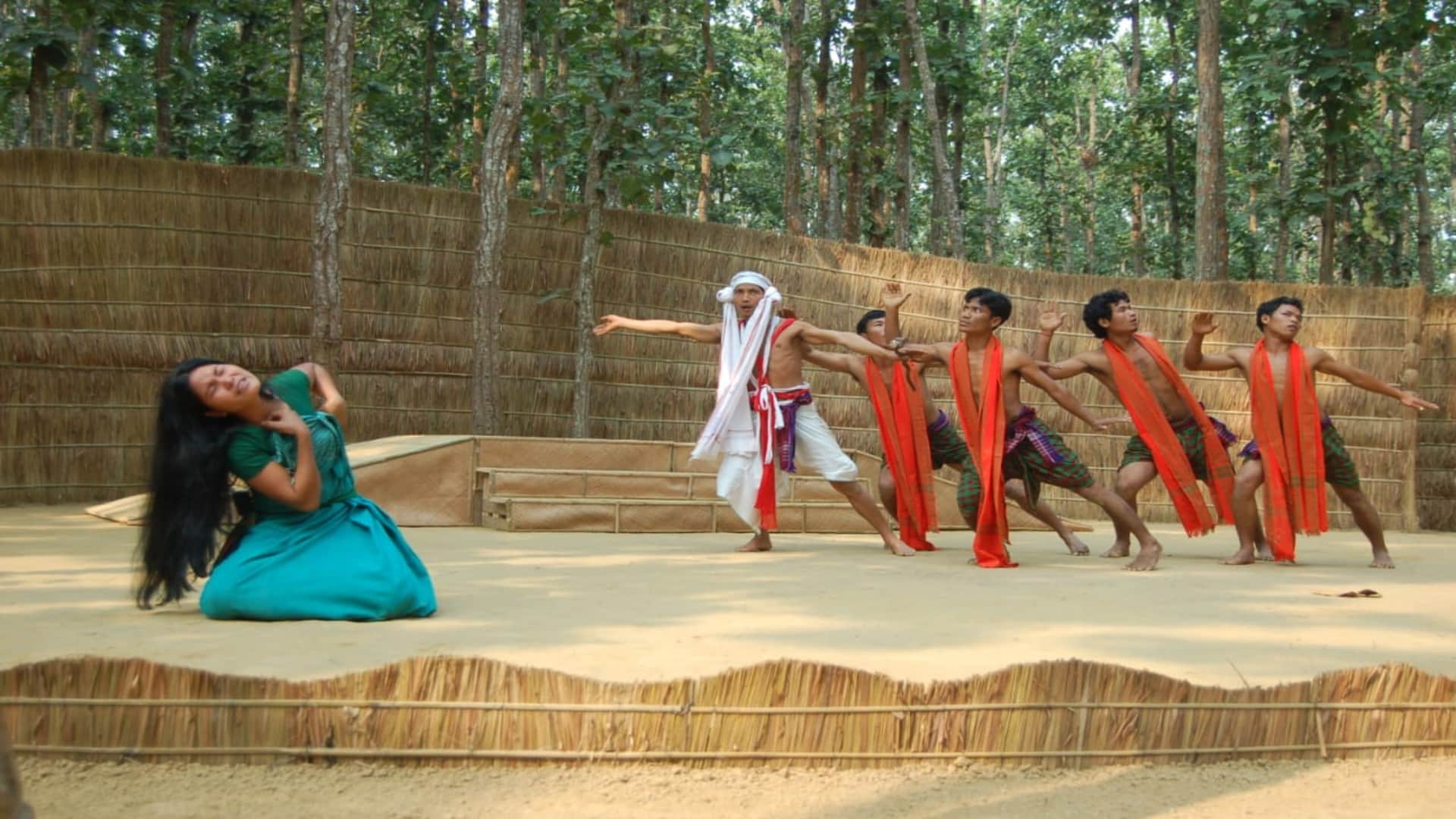 Under the Sal Tree Theatre Festival: Open stage under the trees, audience sits on straw; see picture