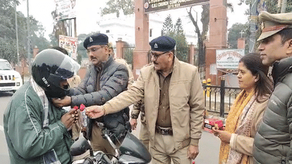 हेलमेट पहनने वाले बाइक चालक को गुलाब का फूल देते यातायात अधिकारी