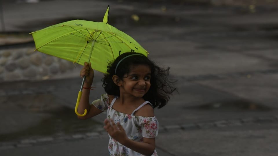 बारिश से बचने के लिए छाता लिए बच्ची।