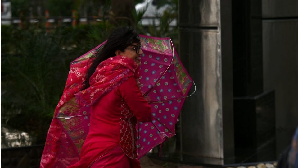 तेज हवा के बीच छाते के साथ गुजरती महिला।