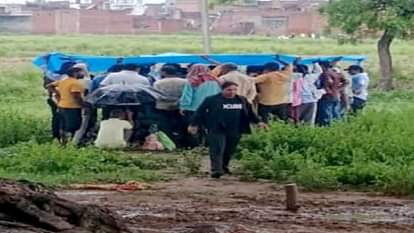 बारिश में तिरपाल लगा कर अंतिम संस्कार करते ग्रामीण