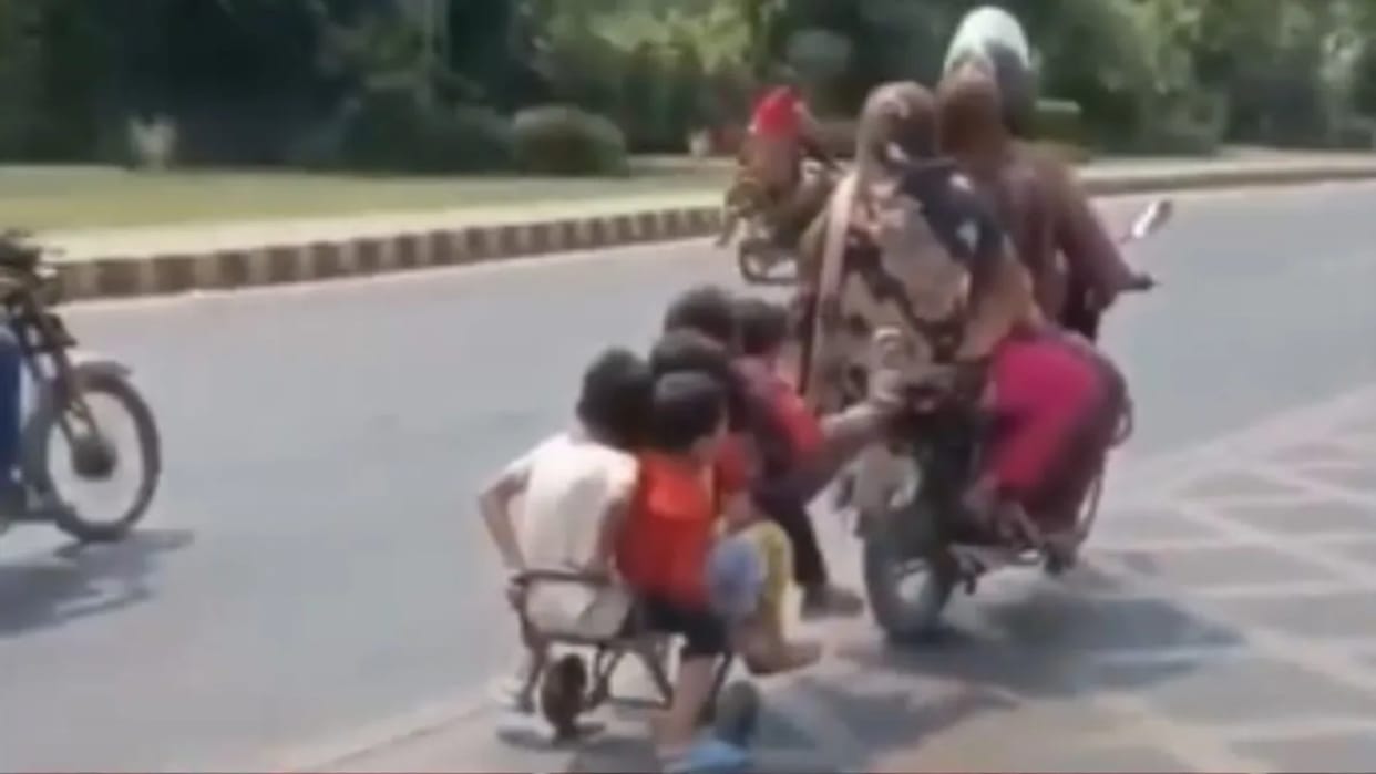 The whole family is sitting on a bike two wives are sitting behind and a group of half a dozen children