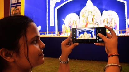 मां दुर्गा की तस्वीर मोबाइल से लेती युवती।