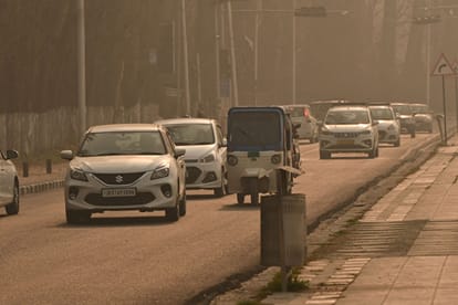 श्रीनगर में सर्द मौसम में धुंध के बीच सड़क से गुजरते वाहन।