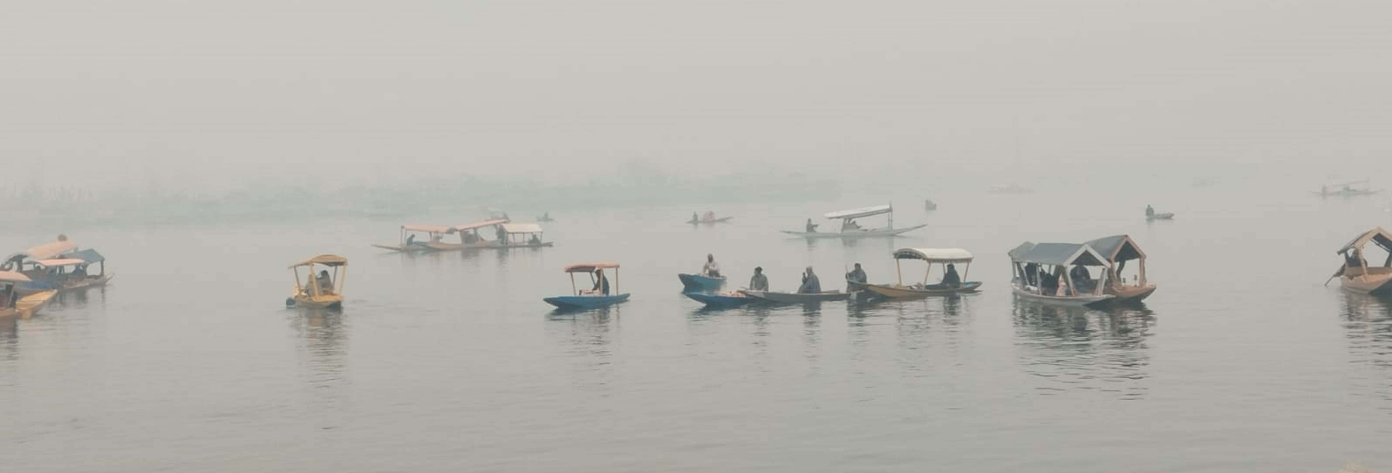 कोहरे के बीच डल झील में शिकारे की सैर करते सैलानी।