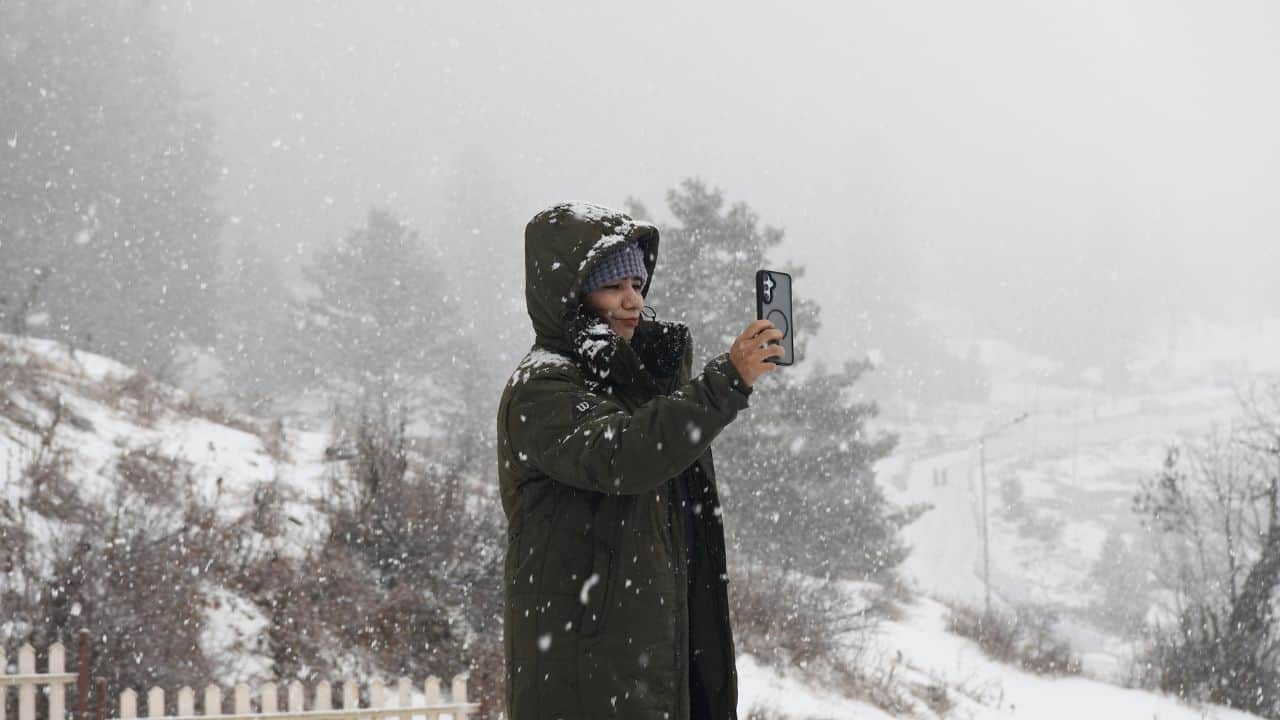 गुलमर्ग में बर्फबारी के बीच सेल्फी लेती महिला पर्यटक।