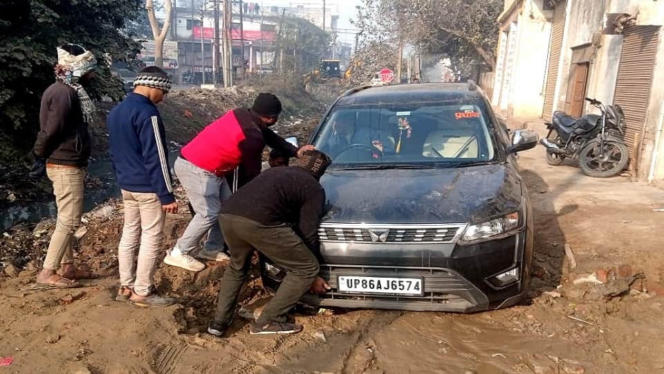गड्ढे में फंसी कार को धक्का देकर निकालते लोग