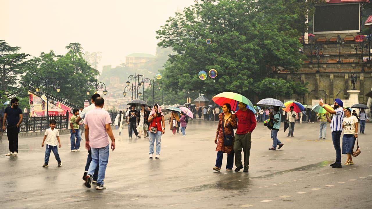 शिमला के रिज मैदान पर छाता लेकर गुजरते लोग।