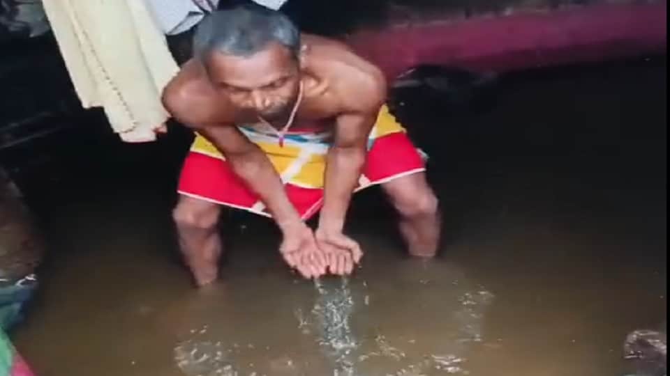 घर में भरा बारिश का पानी निकालता शख्स