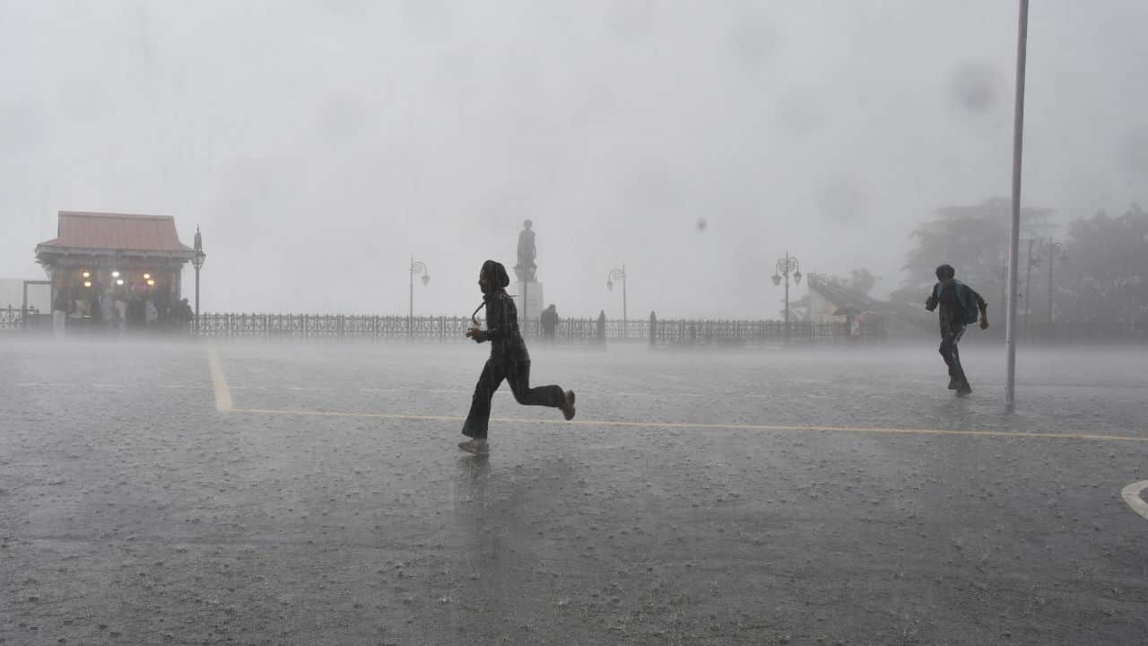 शिमला के रिज मैदान पर बारिश के दौरान गुजरते लोग।