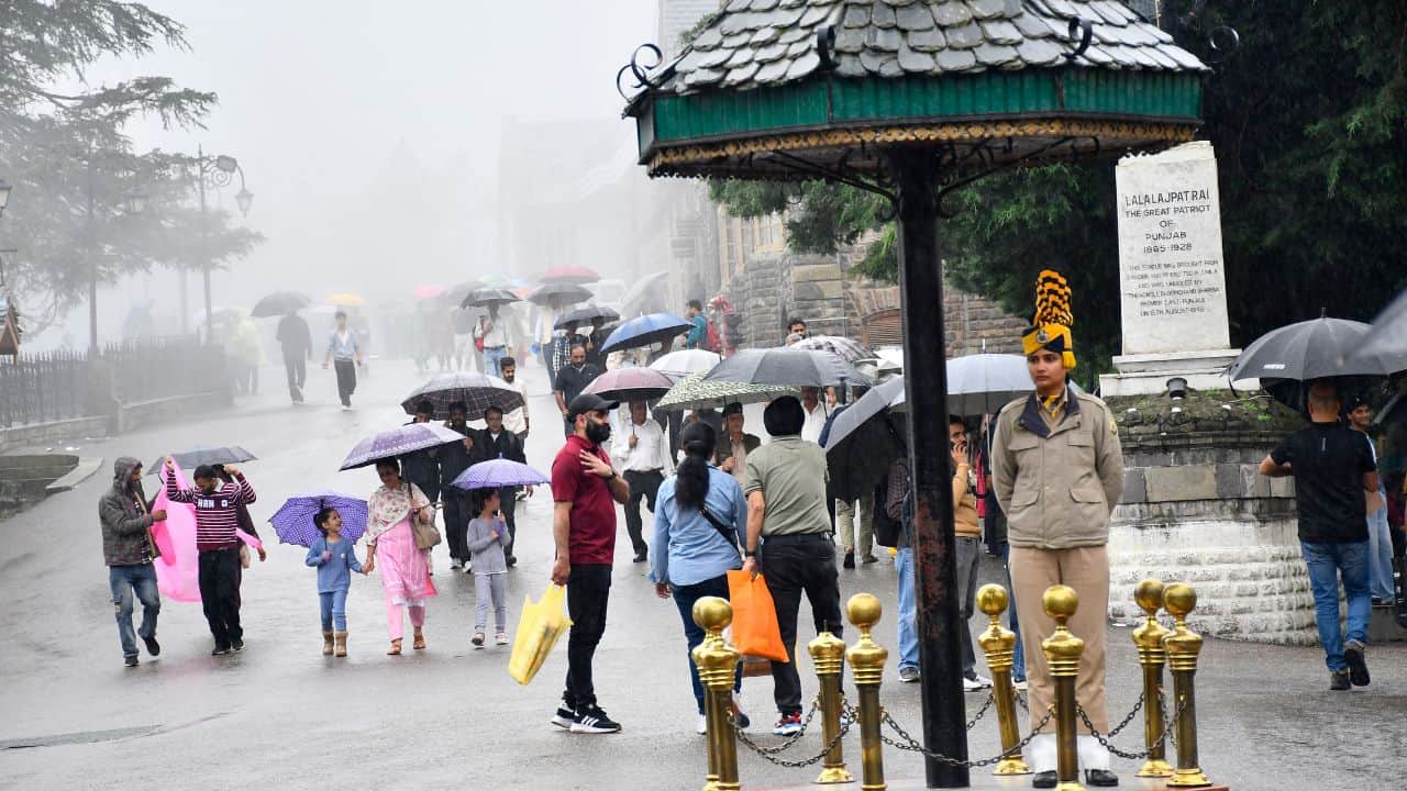 स्कैंडल पॉइंट पर झमाझम बारिश के दौरान गुजरते लोग और ड्यूटी पर तैनात महिला पुलिस जवान।